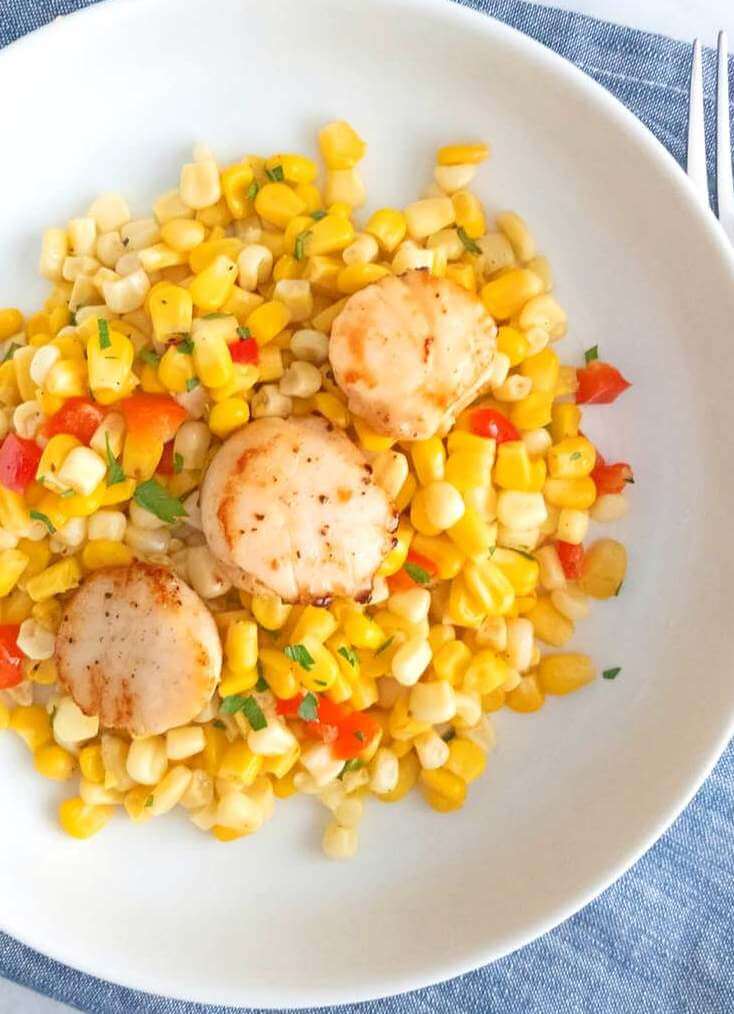 Closeup of Healthy Corn and Red Pepper Salad with Seared Scallops on a white plate.
