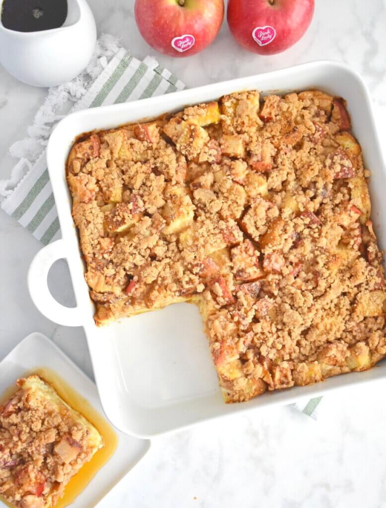 A square baking dish of Pink Lady® Apple Cinnamon French Toast Bake with a slice removed and set on a plate next to it.