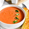 A bowl of tomato soup with fresh basil leaves on top.