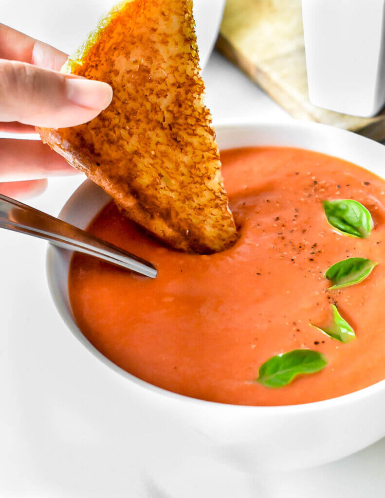 A grilled cheese sandwich being dipped into a bowl of tomato soup.