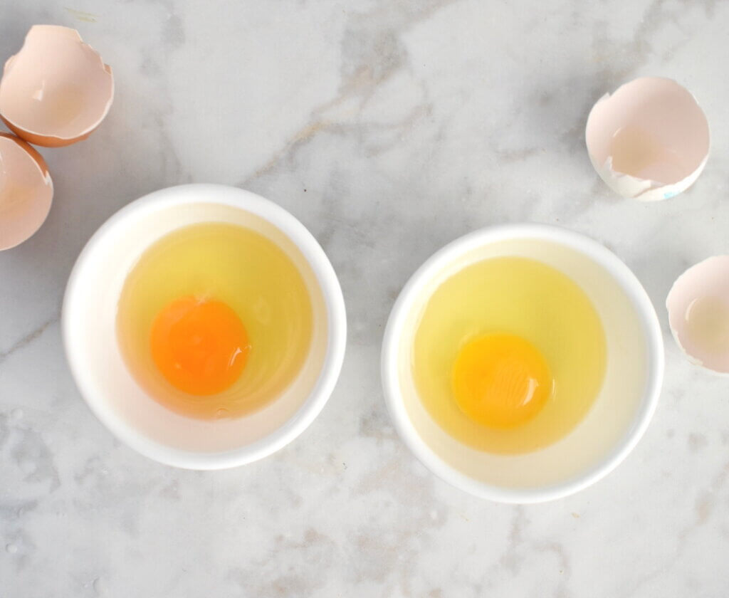 Two cracked eggs in small bowls showing a darker orange yolk from one egg than the other.