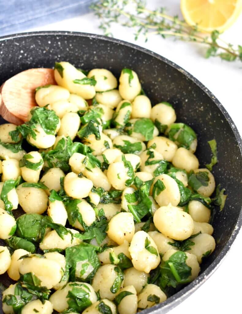 A skillet with gnocchi and swiss chard being stirred by a wooden spoon.