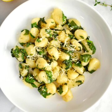 A plate of Gnocchi with Swiss Chard on a table with sliced lemon and fresh thyme.