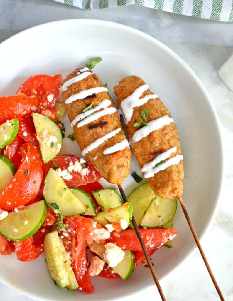 Top view of a plate of Chicken Kofta Kebabs with salad drizzled with yogurt sauce.