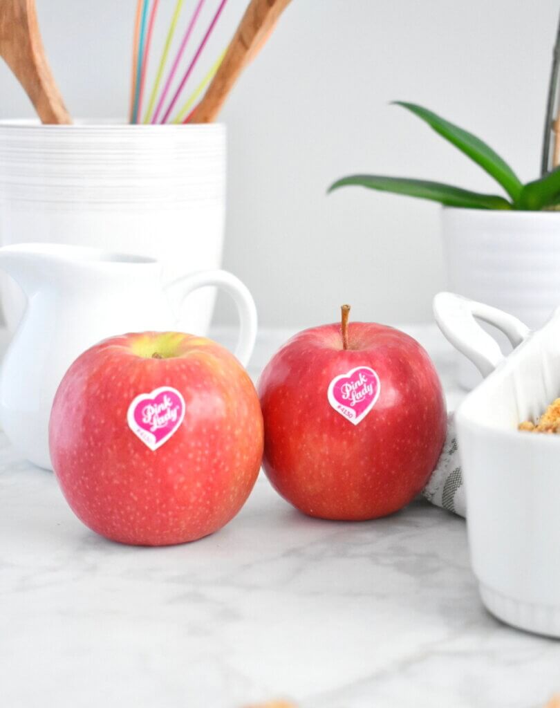 Two pink lady apples set on a kitchen counter.