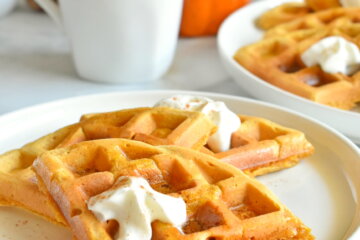 Pumpkin Spice Waffles topped with whip cream on a plate and a cup of coffee.
