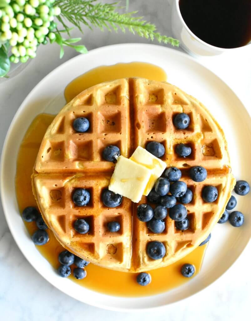 Topview of a stack of waffles with maple syrup, blueberries and butter.
