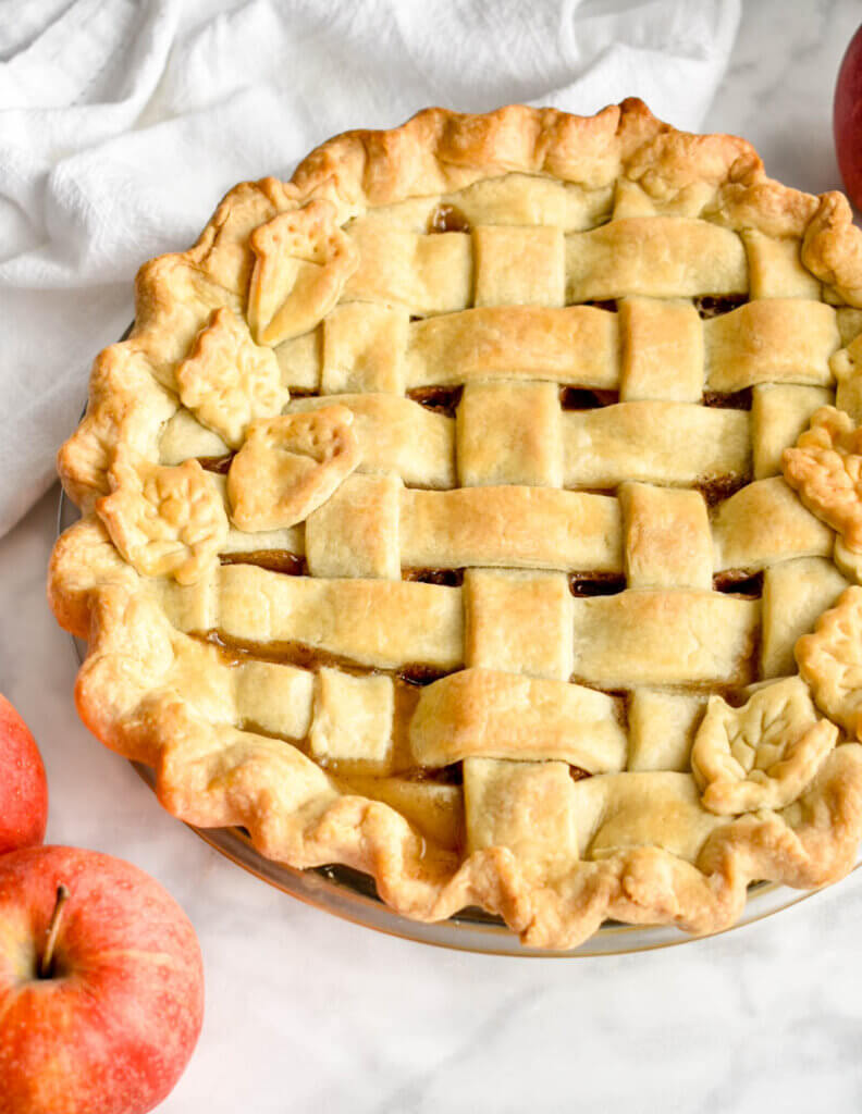 A freshly baked apple pie with a lattice crust on a marble grey countertop.