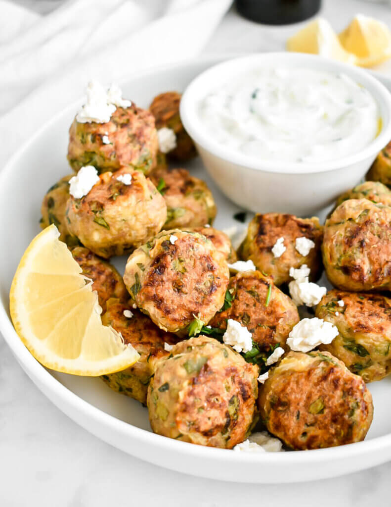 A platter of Greek chicken meatballs made with spinach and feta served with crumbled feta, lemon wedges and tzatziki dip.