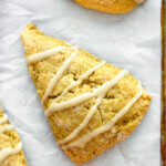A pumpkin scone drizzled with maple glaze set on a tray lined with parchment paper.