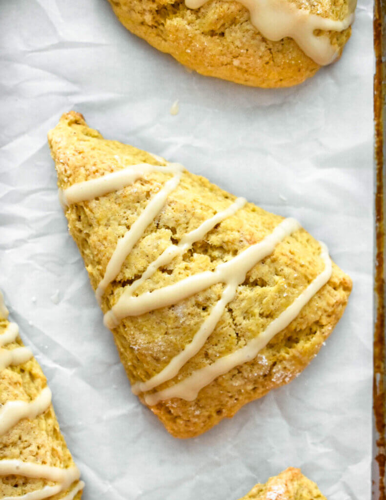 A pumpkin scone drizzled with maple glaze set on a tray lined with parchment paper.
