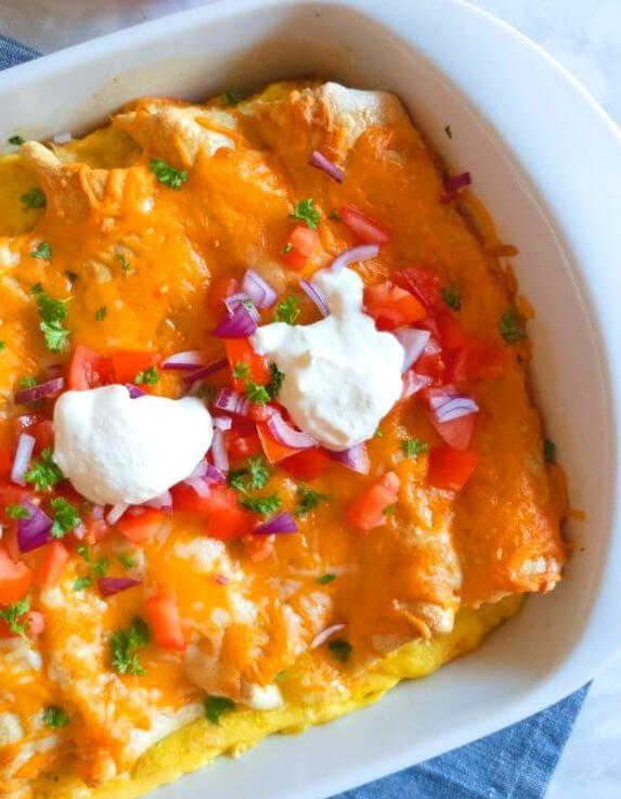 Breakfast Enchiladas closeup with chopped tomatoes and sour cream topping.