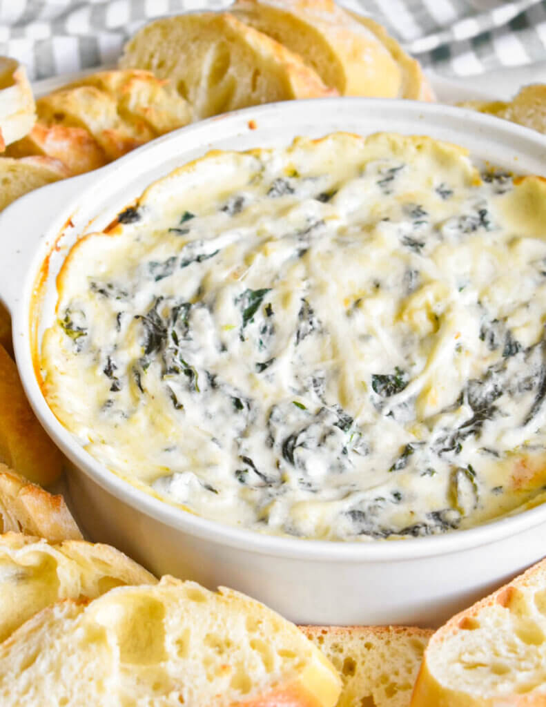 Close up of a bowl of Cheesy Spinach Dip on a platter with bread slices.
