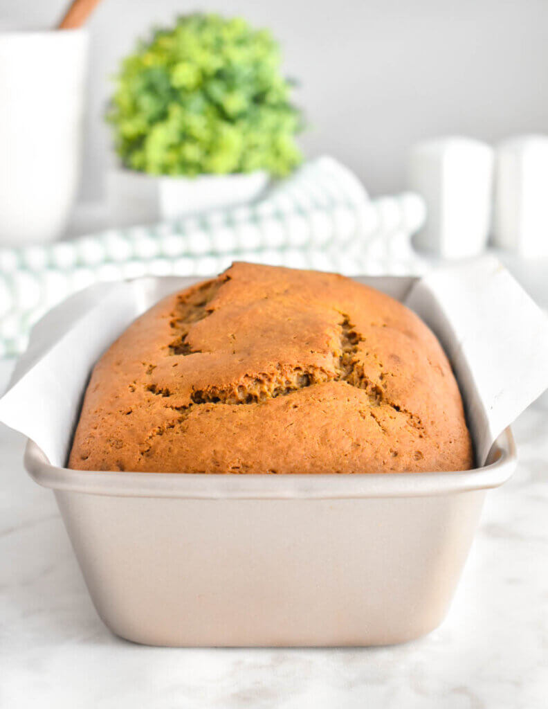A baked loaf of sweet potato bread in a parchment lined loaf pan set on a kitchen counter.