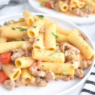 Plates of Creamy Italian Sausage Pasta topped with fresh herbs