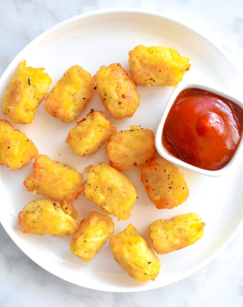 Topview of a plate of tater tots with a bowl of ketchup for dipping.