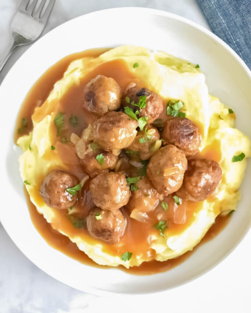 Salisbury Steak Meatballs on top of a pile of mashed potatoes with lots of gravy and fresh herb garnish.