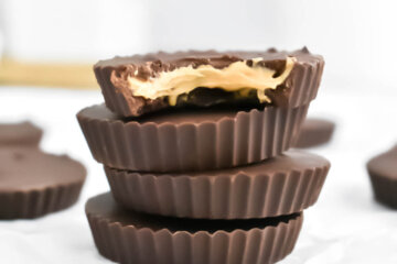 A stack of Homemade Peanut Butter Cups with a bite taken out of the top one, reveal creamy peanut butter center.