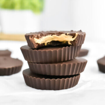 A stack of Homemade Peanut Butter Cups with a bite taken out of the top one, reveal creamy peanut butter center.