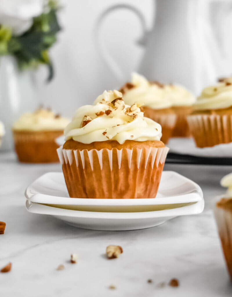 Carrot Cake Cupcake on a dish surrounded by other cupcakes.