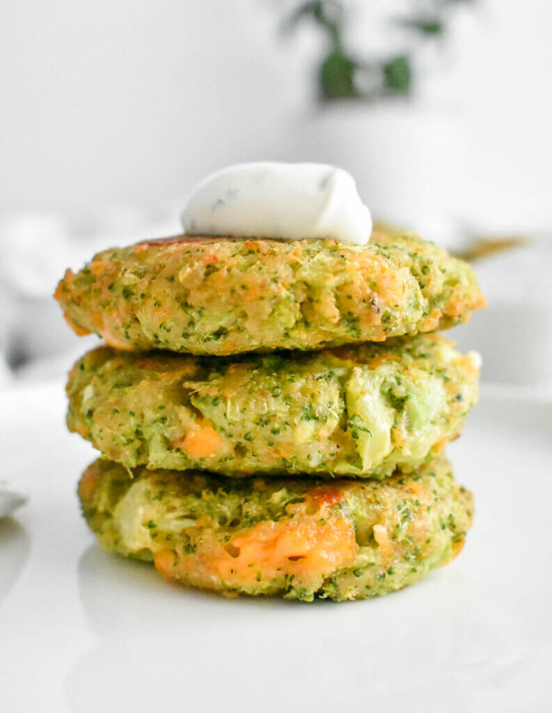 Stack of Cheesy Broccoli Fritters topped with yogurt dip.