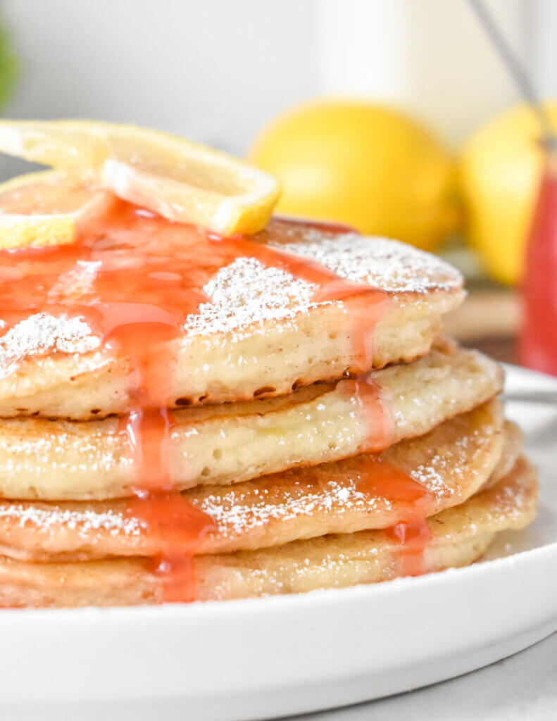 Close up of Lemon Ricotta Pancakes with strawberry syrup dripping down the stack.