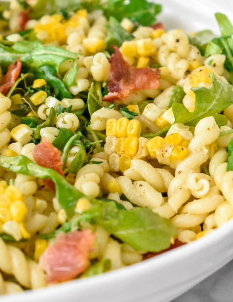 Close up of a bowl of Corn, Bacon and Arugula Pasta Salad showing arugula, pasta, bacon and corn.