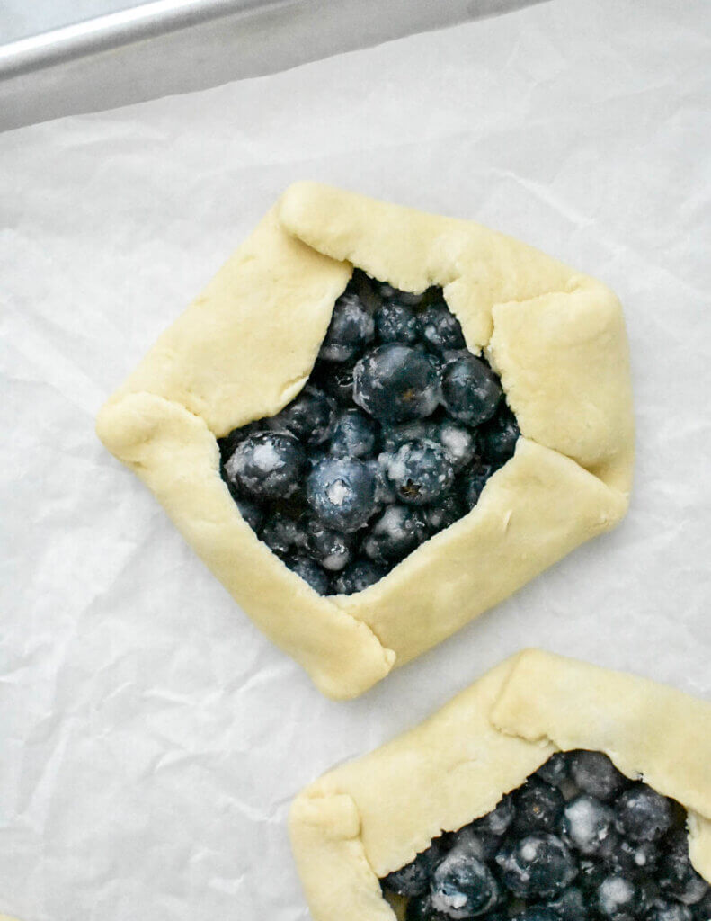 Unbaked Mini Blueberry Galettes on a baking sheet lined with parchment paper.