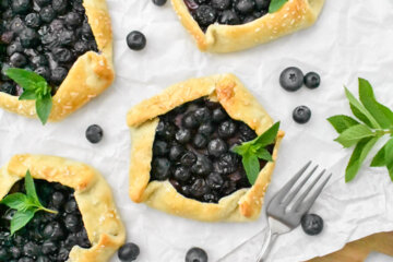 Mini Blueberry Galettes on parchment paper surrounded by fresh blueberries, mint and forks.