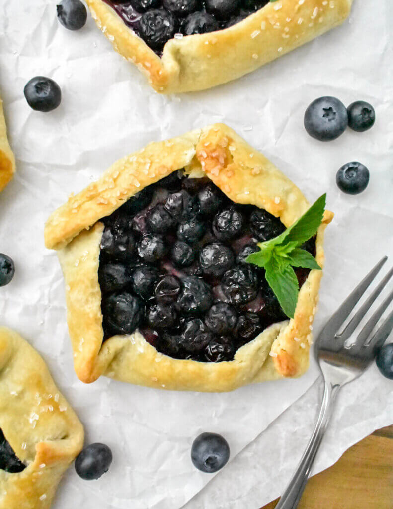 Closeup topview of a Mini Blueberry Galette topped with fresh mint and surrounded by fresh blueberries.