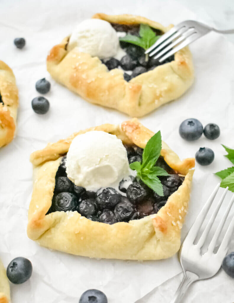 A Mini Blueberry Galettes topped with a vanilla ice cream scoop on parchment paper.