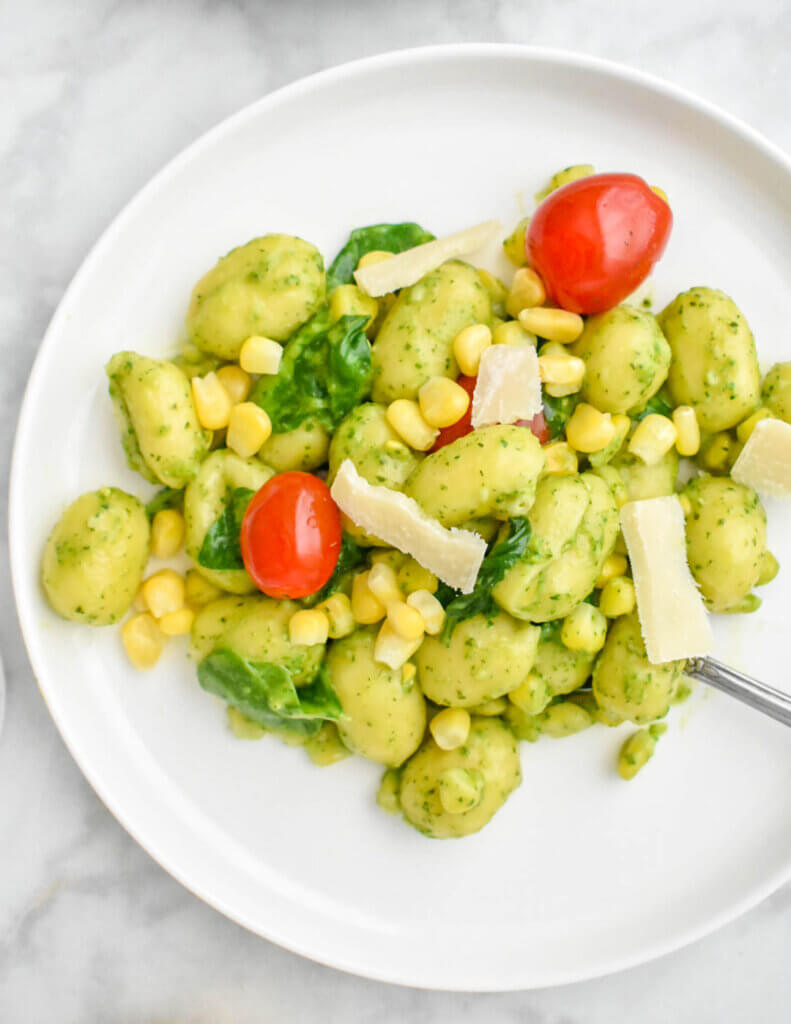 Plate of Summer Gnocchi with Corn, Tomatoes & Pesto topped with shaved parmesan cheese