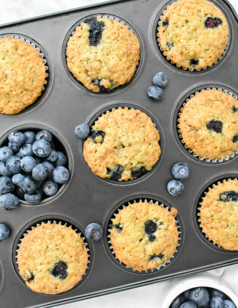 Blueberry Zucchini Muffins in a muffin pan with fresh blueberries