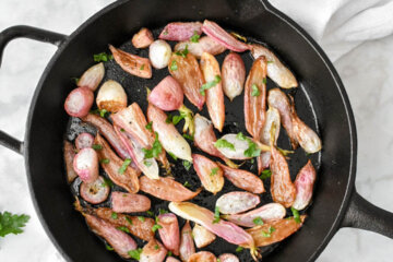 Cast Iron skillet with Roasted Radishes set on a table.