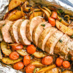 A foil lined sheet pan with roasted pork tenderloin, potatoes and sliced carrots.