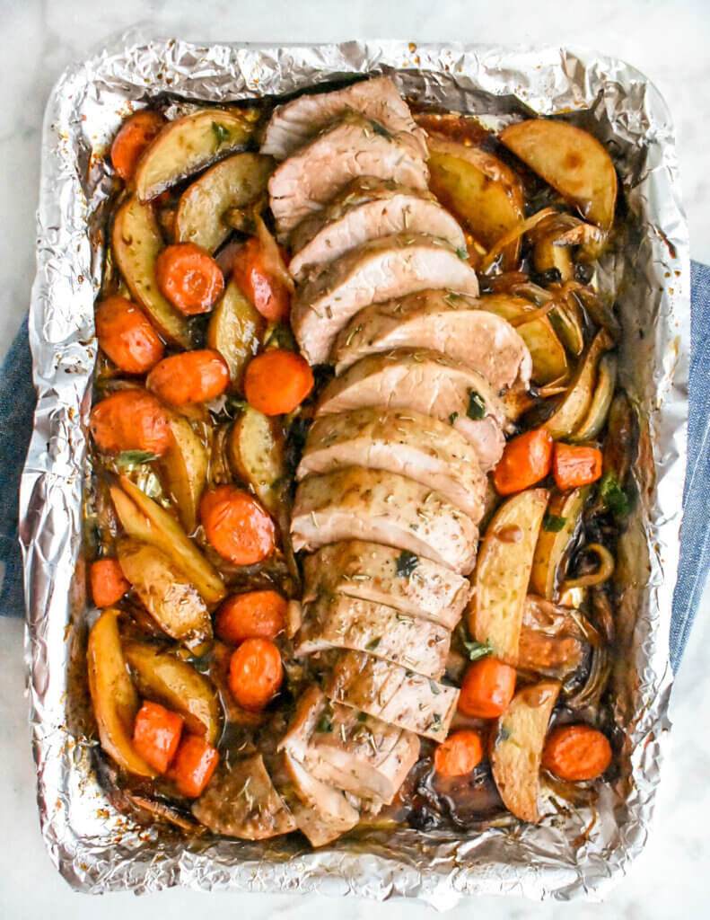 A foil-lined sheet pan with sliced pork tenderloin, roasted potatoes and carrots.