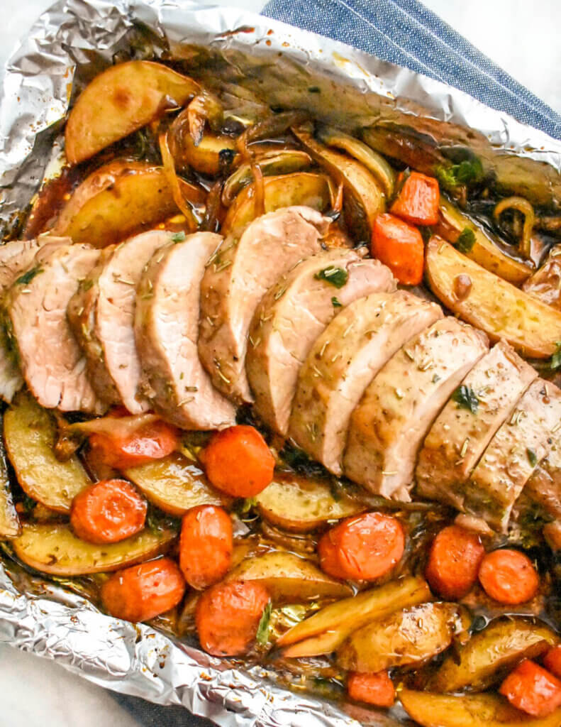 A foil lined sheet pan with roasted pork tenderloin, potatoes and sliced carrots.