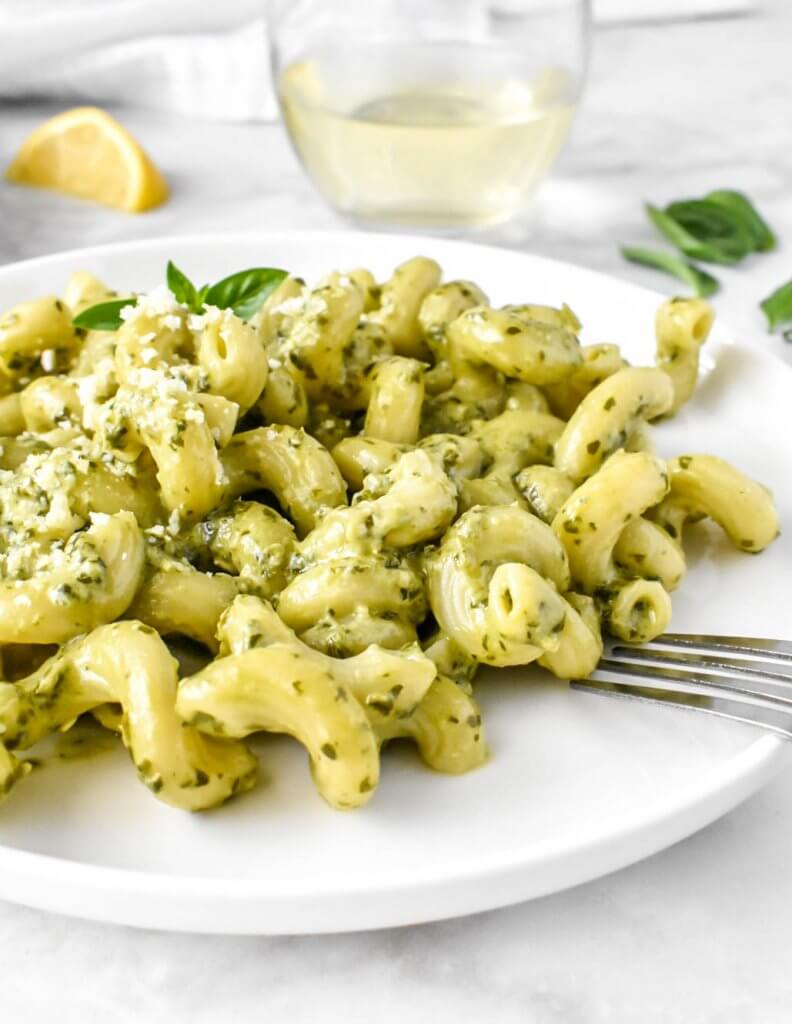 creamy pesto pasta on a white plate and a glass of white wine