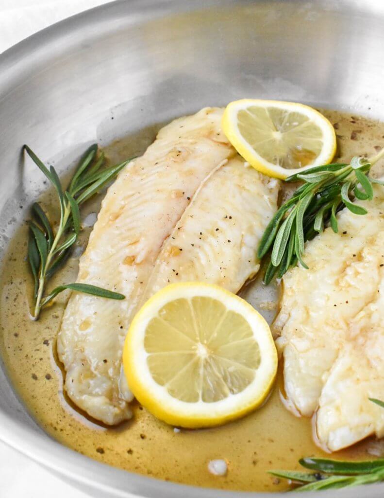 basa fillet topped with lemon slices in a pan with rosemary sprigs