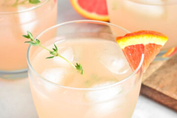 Glasses of Grapefruit & Thyme Gin Fizz garnished with grapefuit segments and fresh thyme