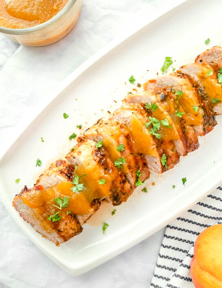 Closeup of sliced pork tenderloin covered in a peach glaze and sprinkled with parsley.