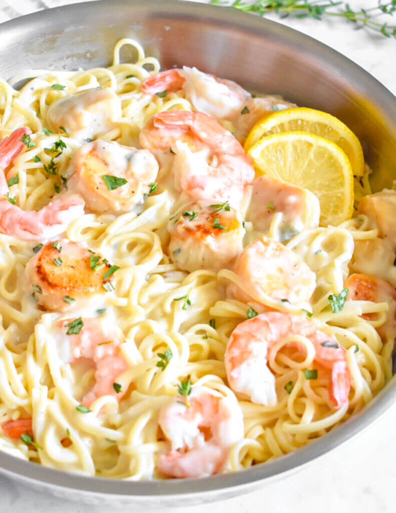 A pan of creamy seafood pasta with lemon slices
