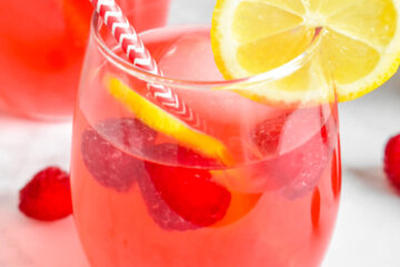 Glass of Raspberry Lemonade topped with fresh raspberries and lemon slices