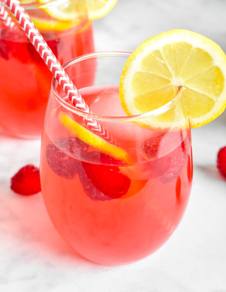 Glass of Raspberry Lemonade topped with fresh raspberries and lemon slices