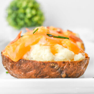 Closeup sideview of a twice baked potato showing the crispy skin, flufy filling and melty cheese.