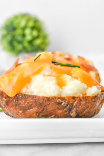 Closeup sideview of a twice baked potato showing the crispy skin, flufy filling and melty cheese.