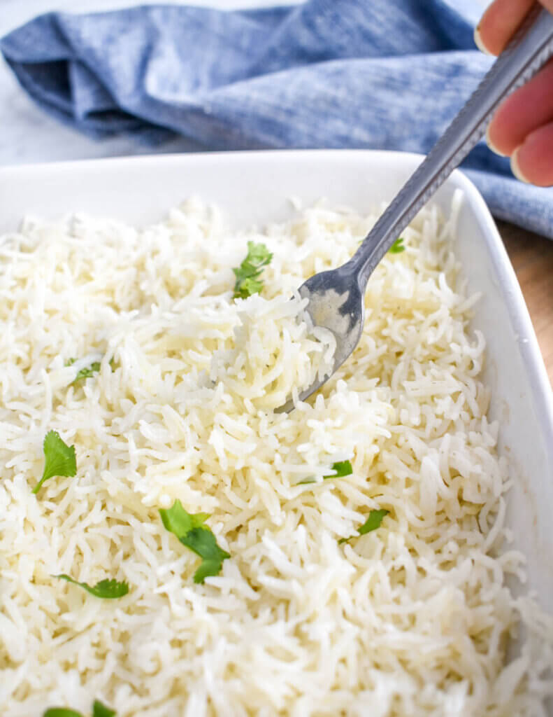 A fork picking up baked coconut rice from a square white baking dish.