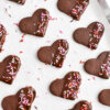 Heart shaped chocolate sugar cookies dipped in melted chocolate and sprinkled with pink, white and red sprinkles.