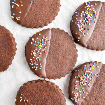 Round chocolate sugar cookies half dipped in chocolate with sprinkles on top.