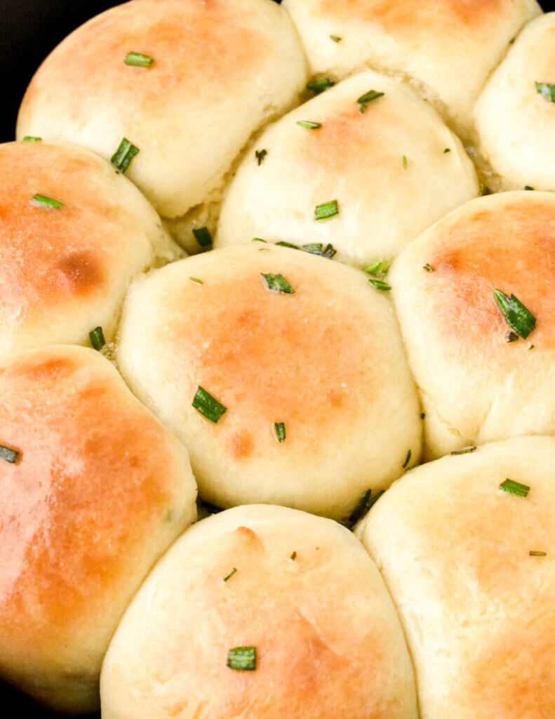 Extreme closeup of baked dinner rolls glistening with melted butter and sprinkled with rosemary.